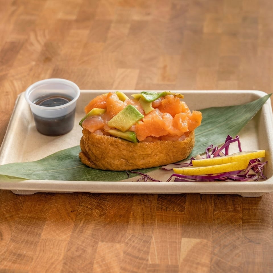 Salmon and avocado poke inari sushi with soy sauce, lemon, and red cabbage on a tray.