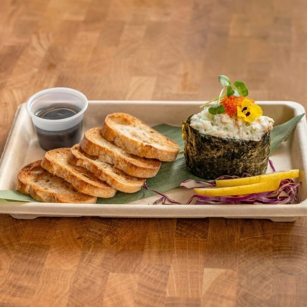 Sushi roll with white filling, topped with orange roe and a yellow flower, served with toast and sauce.