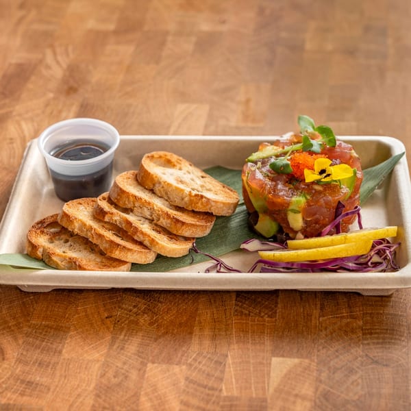 Tuna tartare with avocado, microgreens, edible flowers, and tobiko, served with toasted bread and sauce.