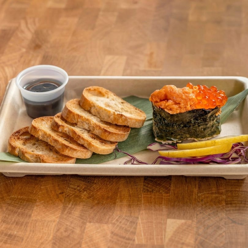 Uni and salmon roe gunkan maki with toasted bread, soy sauce, lemon, and red cabbage.