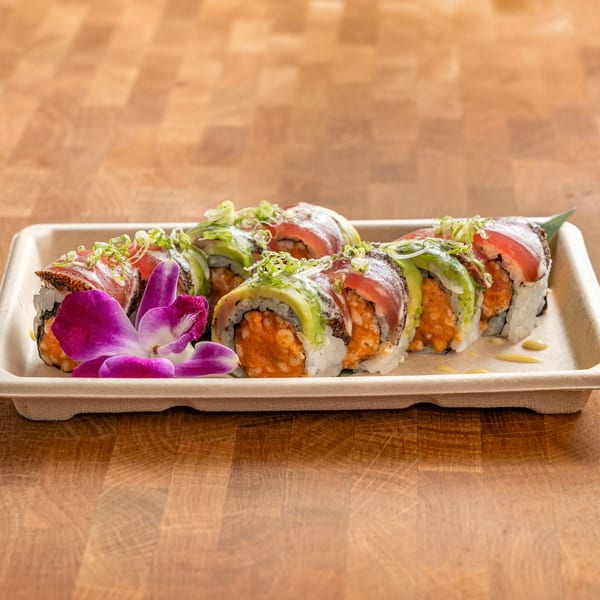 Sushi rolls with tuna, avocado, and spicy filling, garnished with green onions and an orchid.