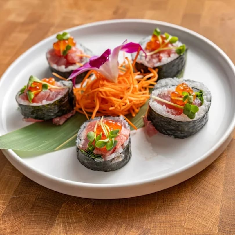 Five tuna sushi rolls with salmon roe, microgreens, and shredded carrots on a white plate.