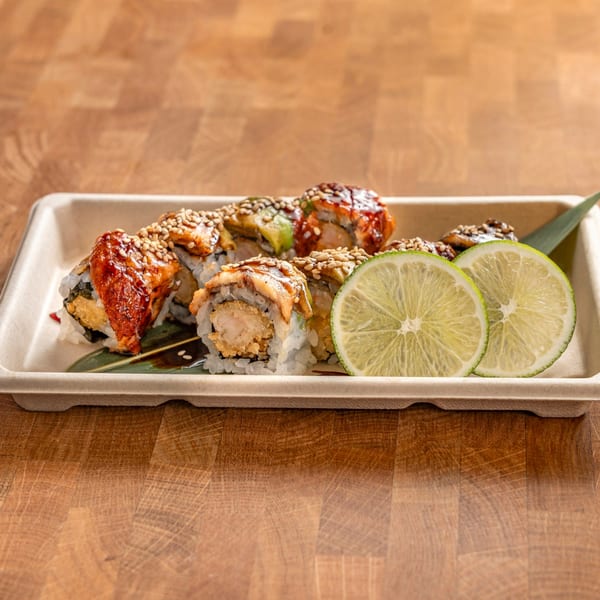 Sushi rolls with eel, shrimp tempura, avocado, sesame seeds, and lime slices in a tray.