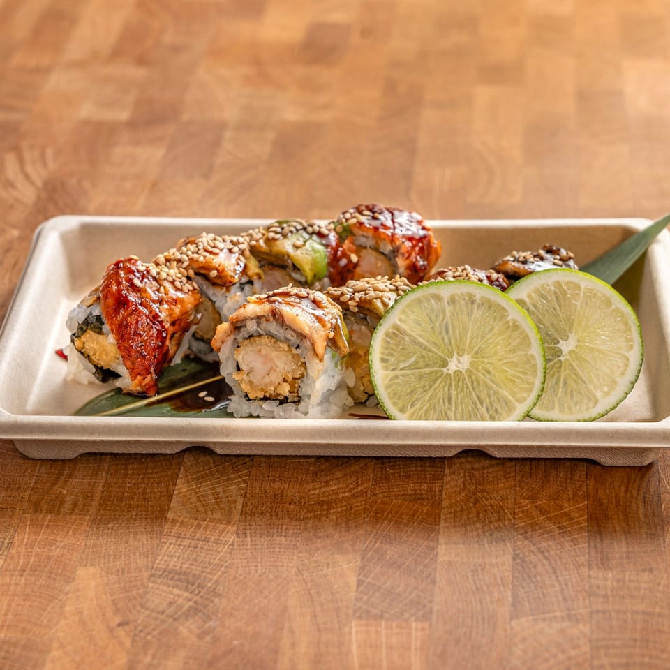 Sushi rolls with eel, shrimp tempura, avocado, sesame seeds, and lime slices in a tray.